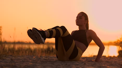 Young-beautiful-woman-athlete-practicing-on-the-beach-doing-exercises-for-the-muscles-of-the-abs-at-sunset.-Twisting-in-slow-motion